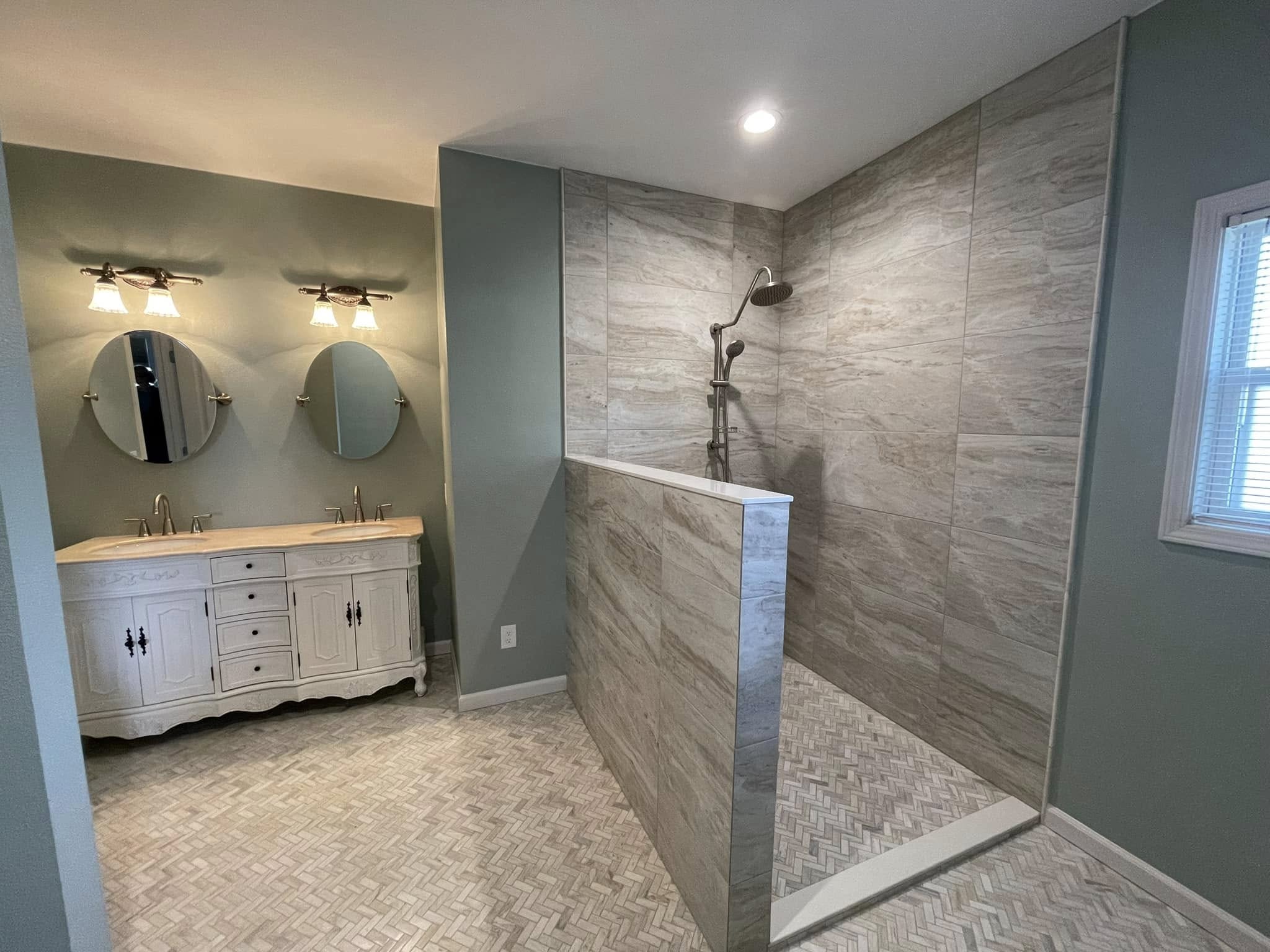 Completed master bath featuring a tiled walk-in shower, half wall, patterned floor tile and double vanity.